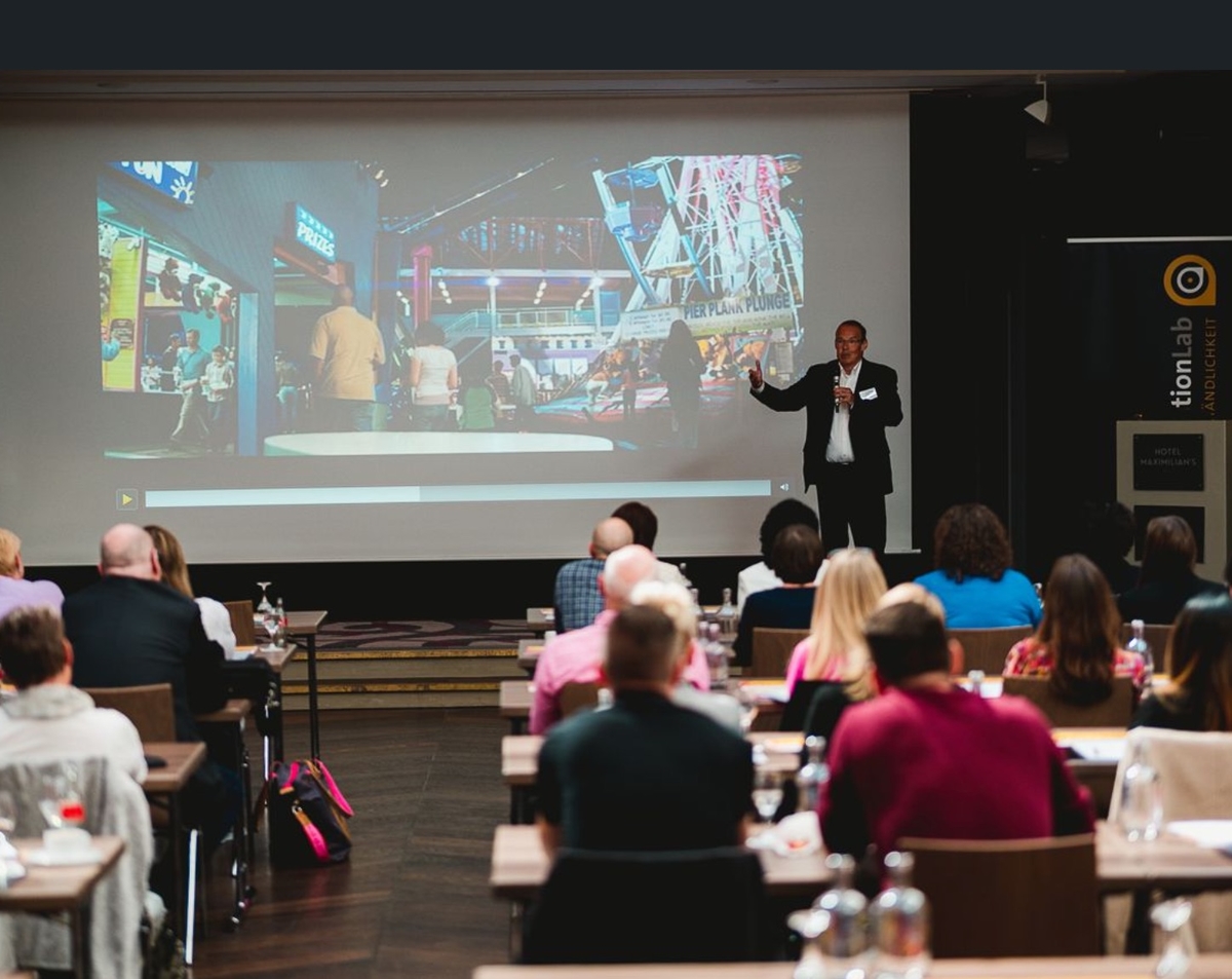 Bild: Prof. Dr. Christian Zielke als Keynote-Speaker vor begeistertem Publikum. Fesselnde Bilder und Filme auf großer Leinwand im Hintergrund.