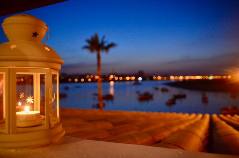 Bild: Die Kraft der Stille - Leuchtende Lampe im Abendlicht mit Kerzenschein, Hafen mit vielen kleinen Booten im Hintergrund. Erfahren Sie mehr über Prof. Dr. Christian Zielke und seine Betrachtung von Ruhe und Besinnung